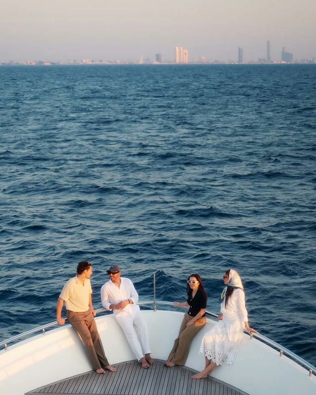 Four friends talking on the bow of a boat at sunset, a city skyline across the water