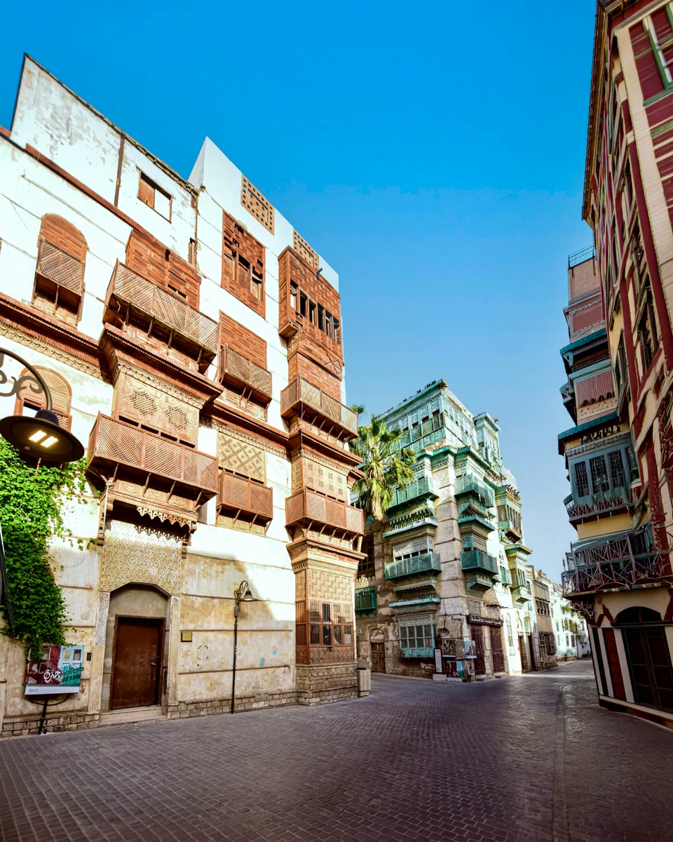 A street in Al-Balad under a blue sky, coral stone houses with carved wooden roshan balconies